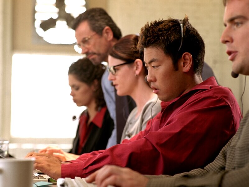 Stock photo of group of people training on keyboards, focusing on a screen (not pictured)